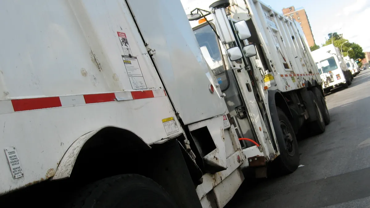 A row of garbage trucks are lined up and parked.
