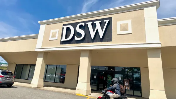 A person on a motorcycle wearing a helmet rides by a store with pillars.