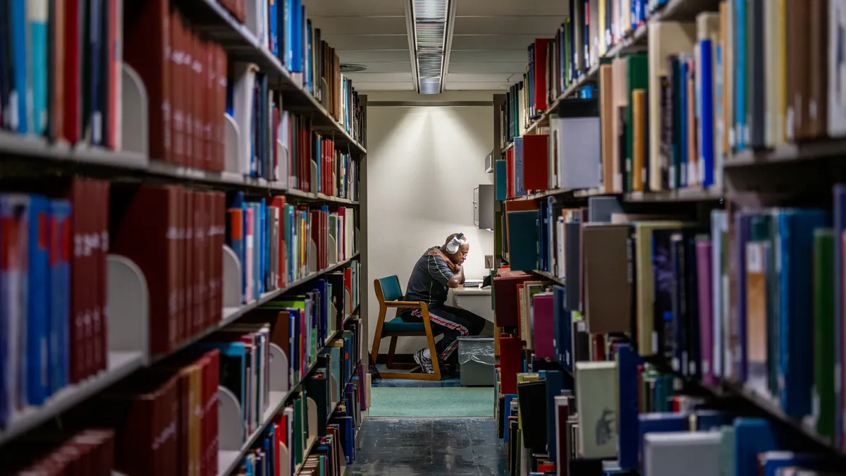 A person sits at a table, framed by two rows of full bookshelves.