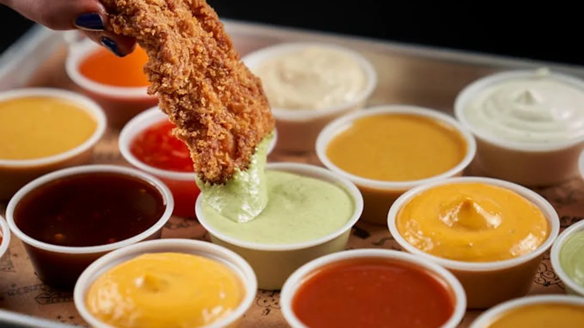 A hand dips a chicken tender into a dipping sauce.