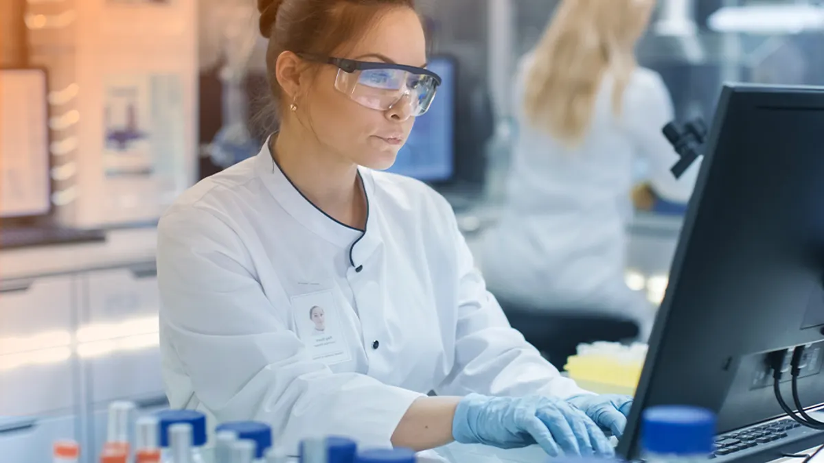 woman wearing a lab coat and gloves working on a desktop computer