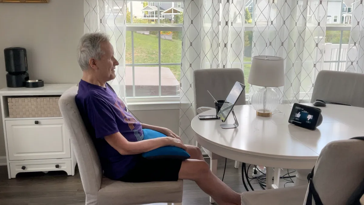 A man sits at a table using Synchron’s BCI platform to control Amazon's Alexa.