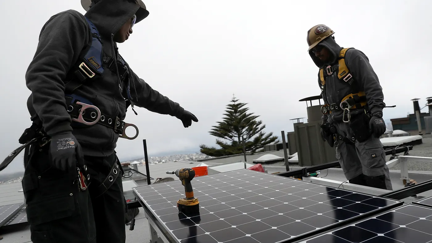 A worker points to a solar panel while another worker looks on.