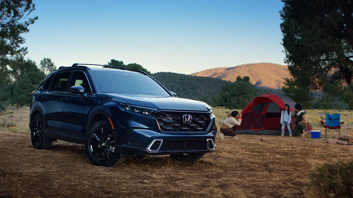 A car is parked next to a camping tent and several people.