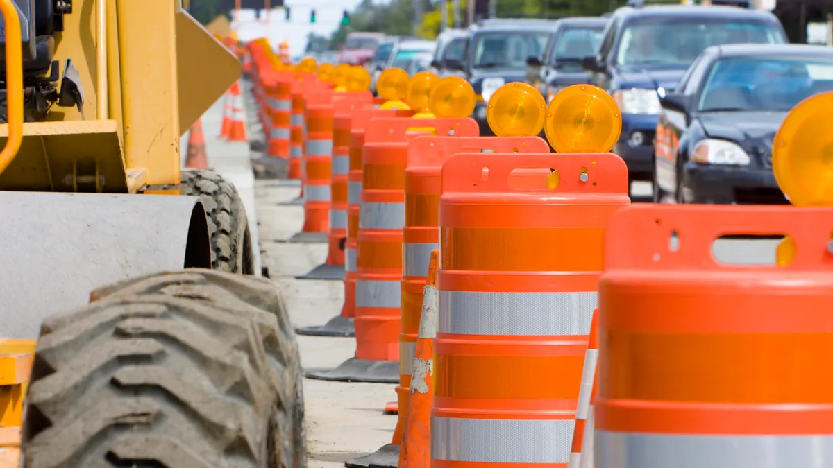 A row of bright Orange construction barriers separate construction from the busy traffic.