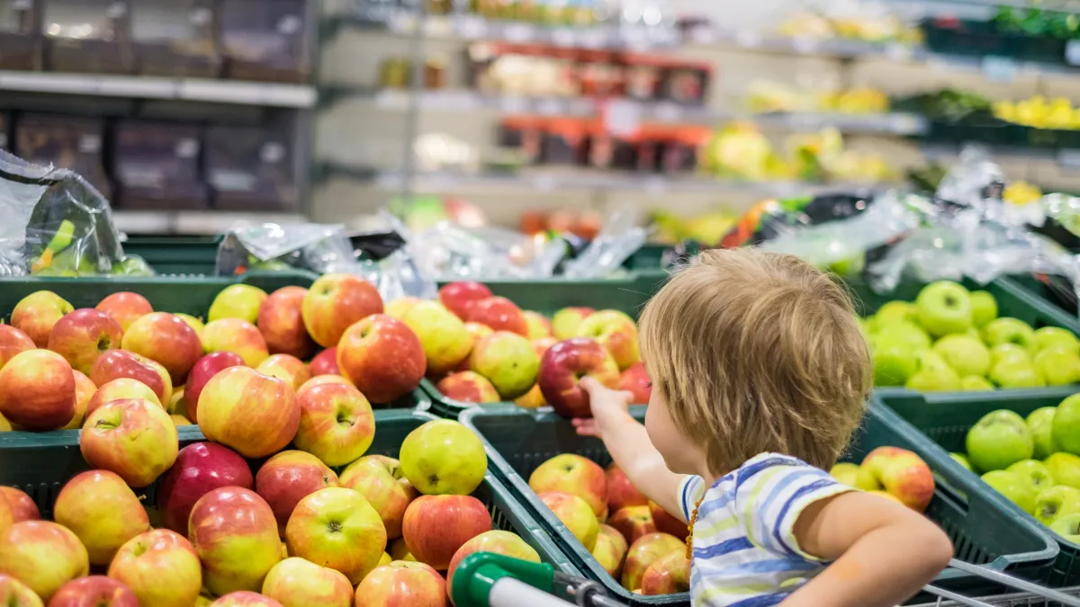 A child grabbing an apple inside of a store.