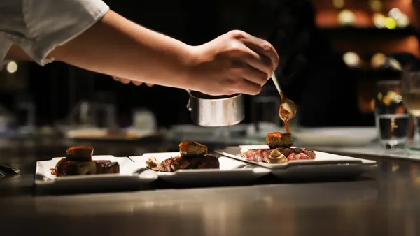 A hand drops sauce from a spoon onto plates of food.