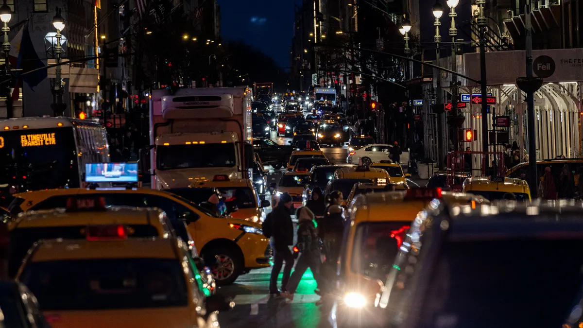 Nighttime view of congested Midtown Manhattan street with people walking across.