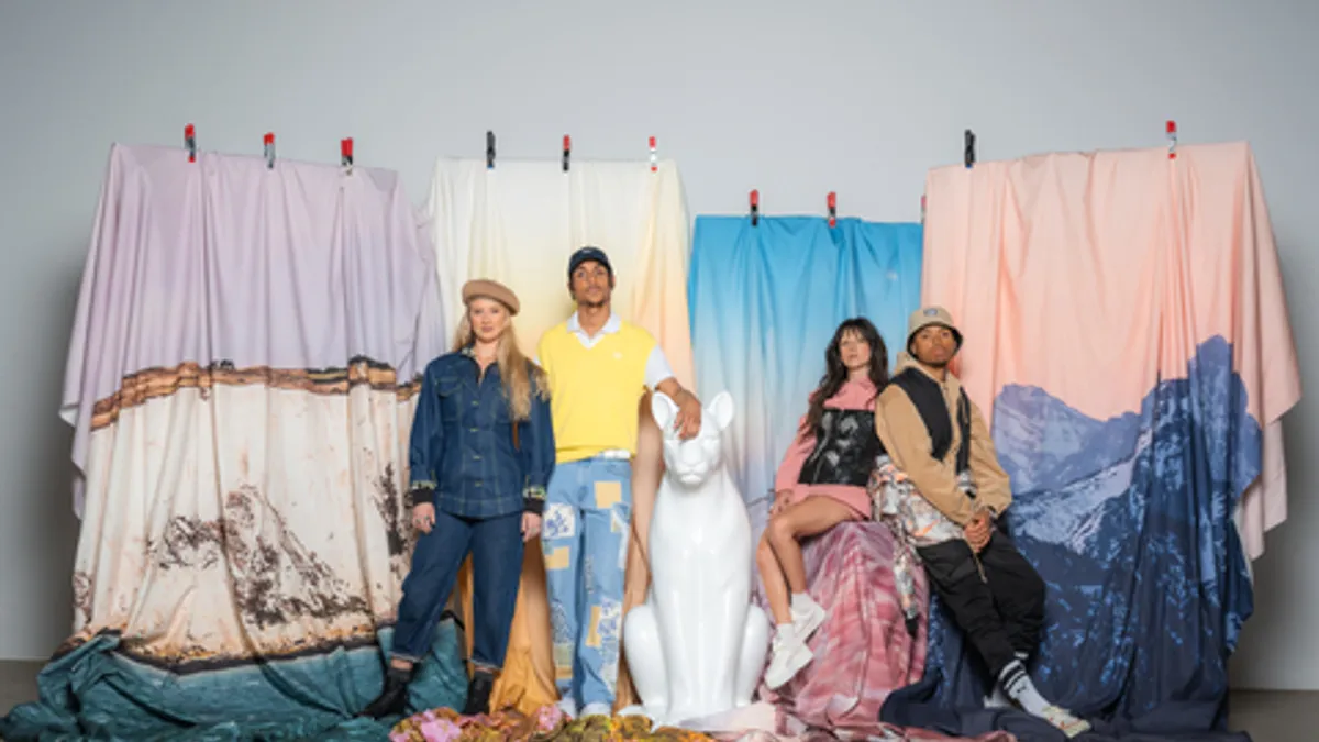 A group of young people stand in front of multicolored range of fabric.