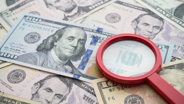 A red magnifying glass sits on top of cash.
