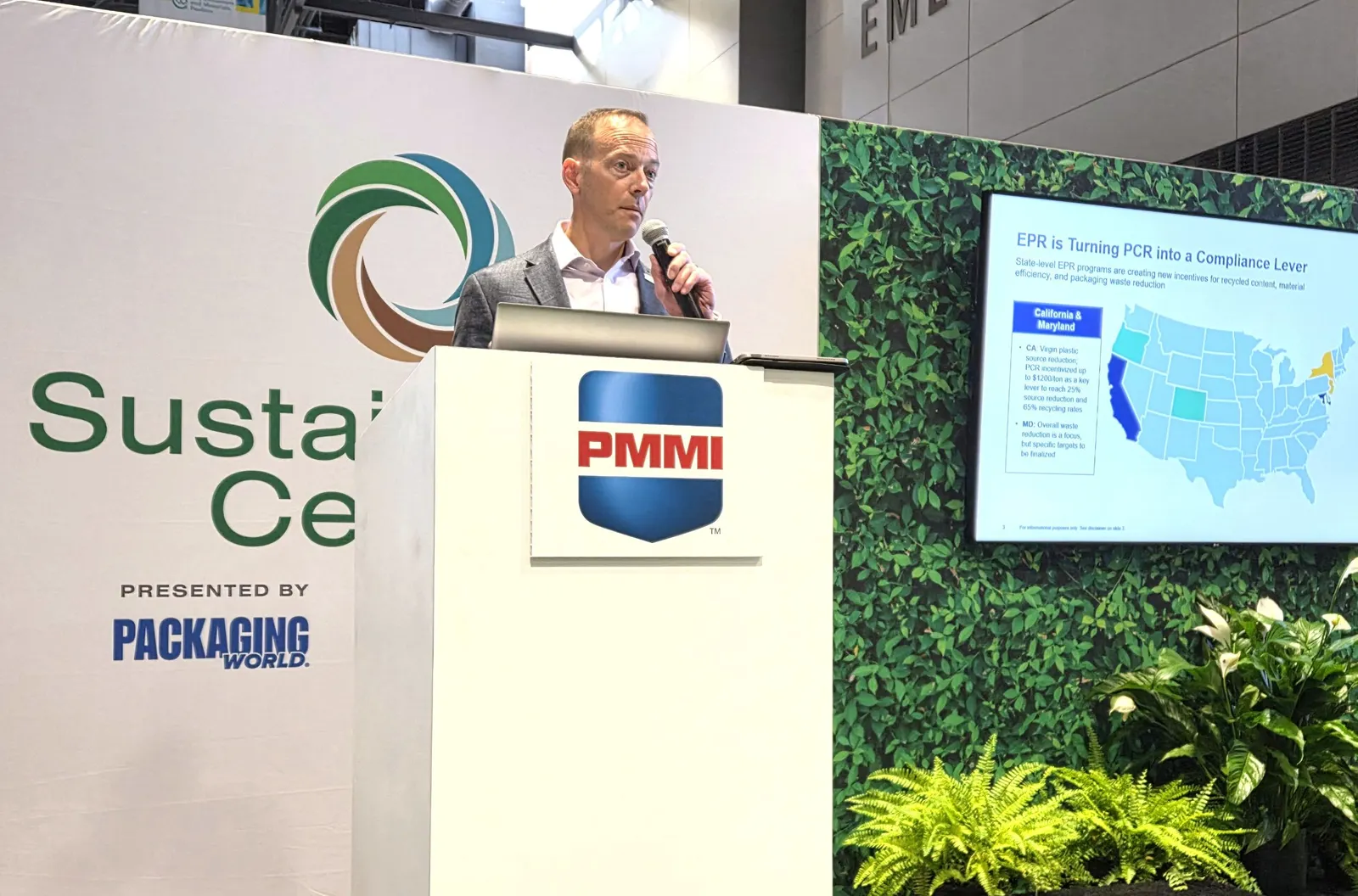 A person holding a microphone stands at a podium with a PMMI logo on it.