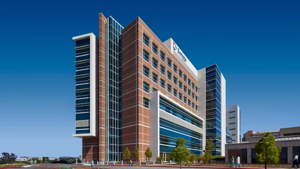 A tall, glass-covered building stands against the backdrop of a blue sky, with not much other development around it.