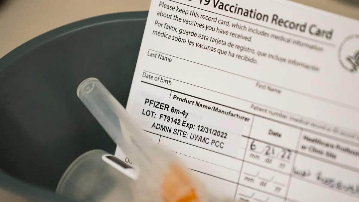 A COVID-19 vaccination record card sits in a container along with a syringe.