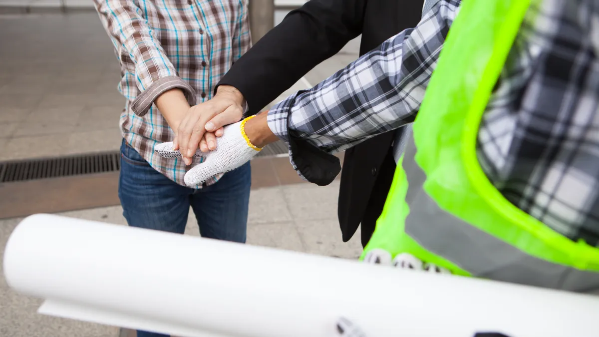 Workers put hands together in the center of a circle on a construction site.