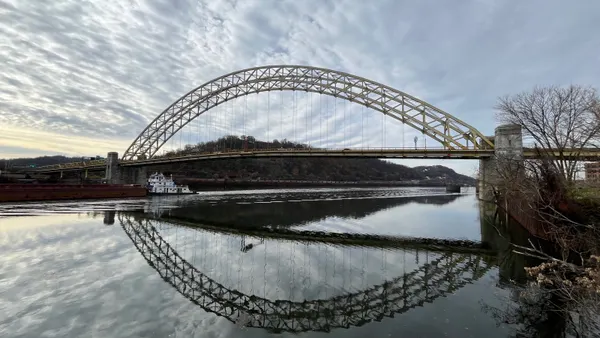 A bridge looms in the background over a river with some foliage on either side of the river.