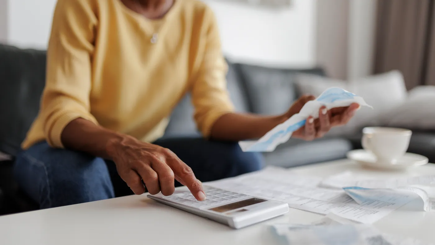 Close up of a person with a calculator and holding a bill.