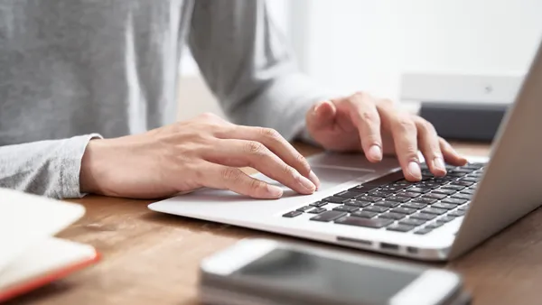 A person in a grey sweater hovers over a laptop with their hands.