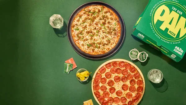 An image of two pan pizzas in front of a green background. On the right is a green pizza box.