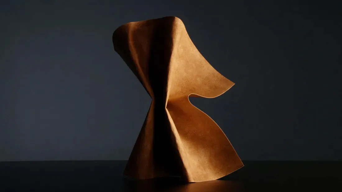 Sculptural image of tan leather-like material folded against dark background.