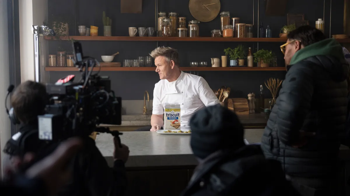 Gordon Ramsay in chef's attire sitting behind a box of Triscuit crackers.