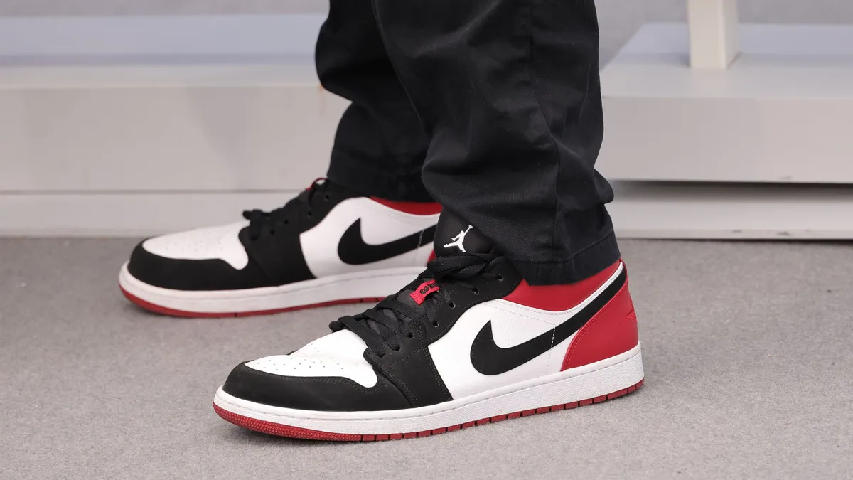 A closeup shot of a person wearing red, white and black sneakers with a Nike logo and black track pants with a Jordan logo.