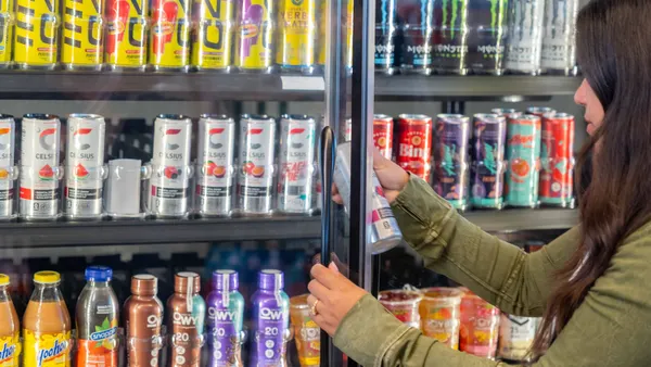 A photo of a number of beverages in a cooler case inside a store. some of the cans say Celsius, Monster and C4.