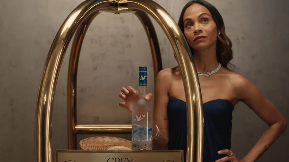 Zoe Saldaña holds a bottle of Grey Goose on a luggage cart.