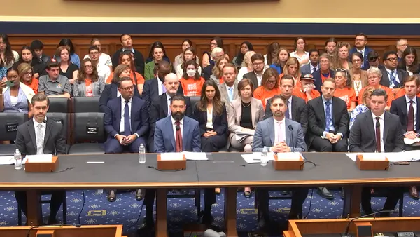 Four men in suits sit behind a row of desks facing members of Congress.