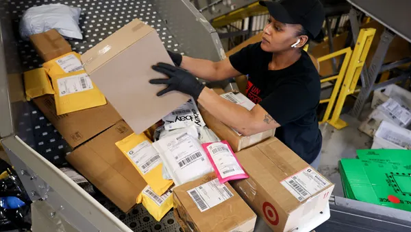A person picks up and inspects a package from a pile on a conveyor belt.
