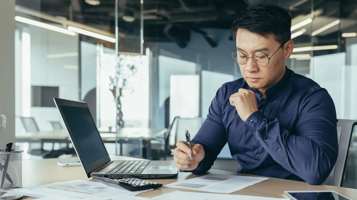 Person working as desk with papers and laptop.
