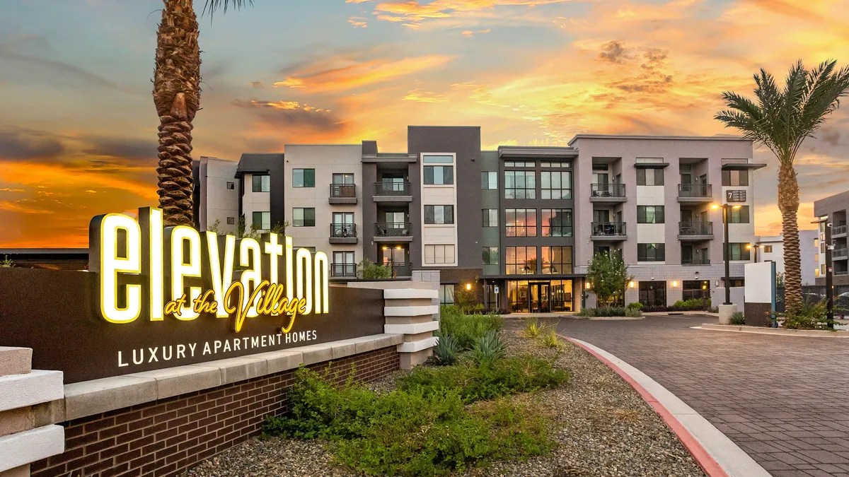 Elevation at the Village sign with four-story brown and tan apartment and brown apartment on the background