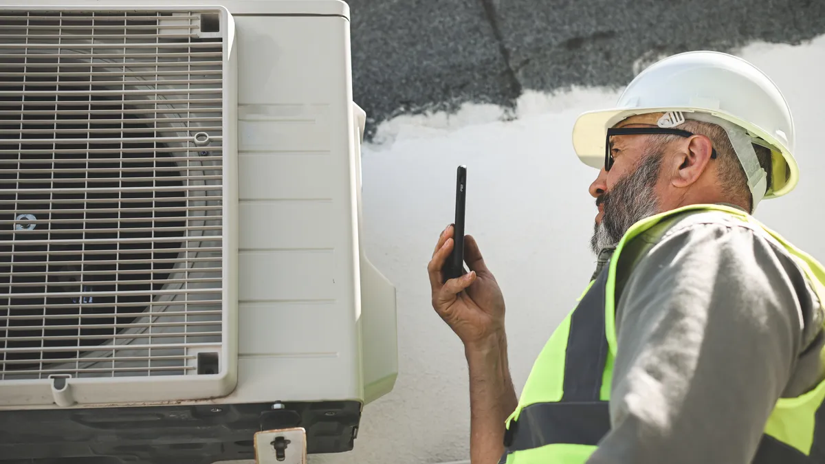 An engineer uses his phone to help repair an air conditioner.