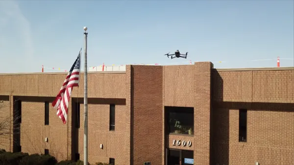 A drone flies over a brick building with 1600 over the door and U.S. flag on flagpole in front.