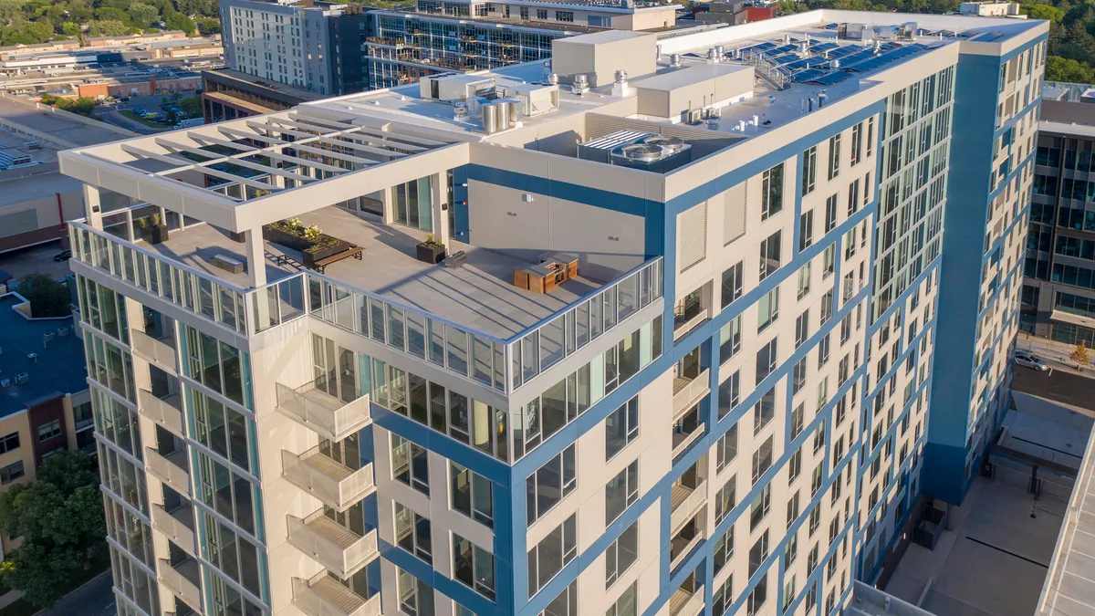 A midsize glass apartment building, angled toward the rooftop, with solar panels and a deck in view.