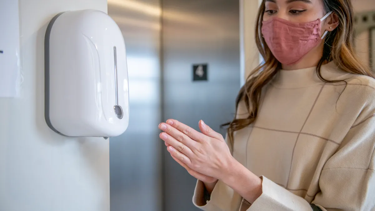 A person sanitizes their hands and wears a mask