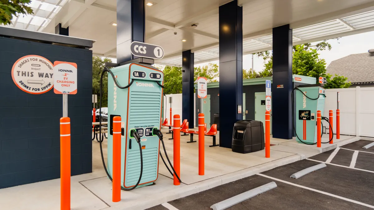 An outdoor IONNA EV charging hub showing orange bollards and two multi-vehicle chargers painted light blue.