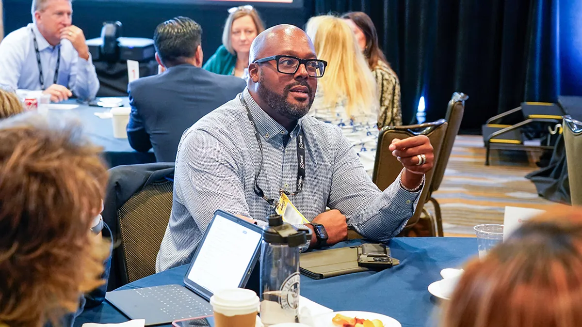 a person's hand with a silver ring on the ring finger, gesturing during a conversation at a conference table.