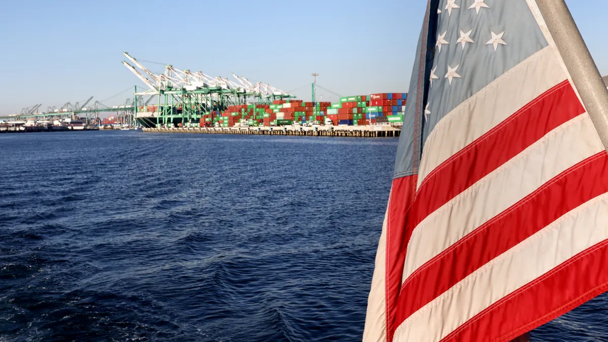 An American flag flies from a ferry passing near shipping containers stacked at the Port of Los Angeles on November 24, 2021.