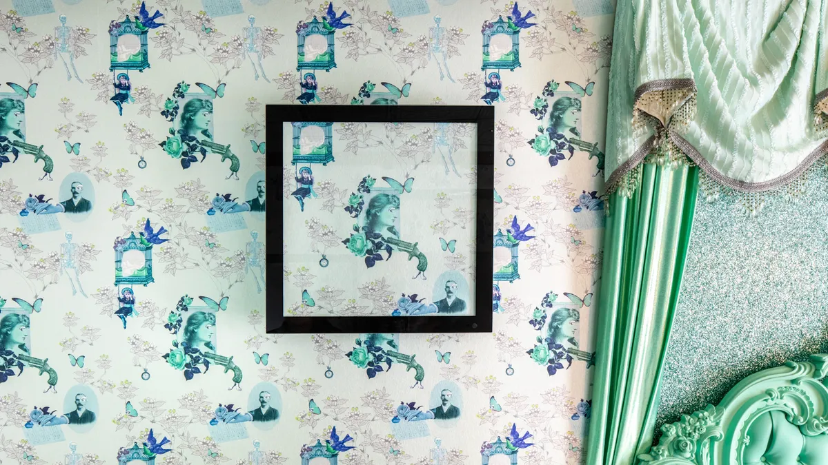 A black frame surrounds a blue-green flower pattern that is also featured on the wallpaper behind it.