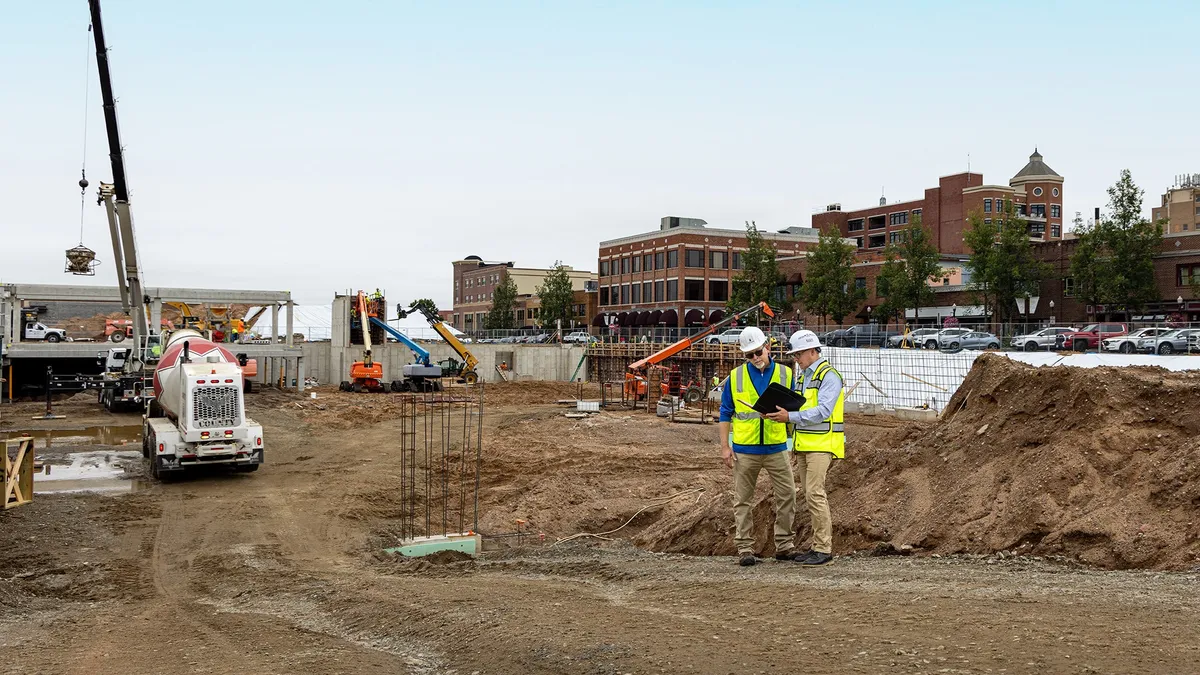 Two people stand on a jobsite surveying.