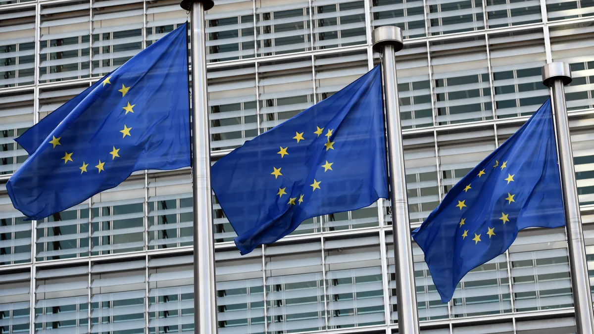 Blue and yellow flags bearing the European Commission logo fly in front of a building.