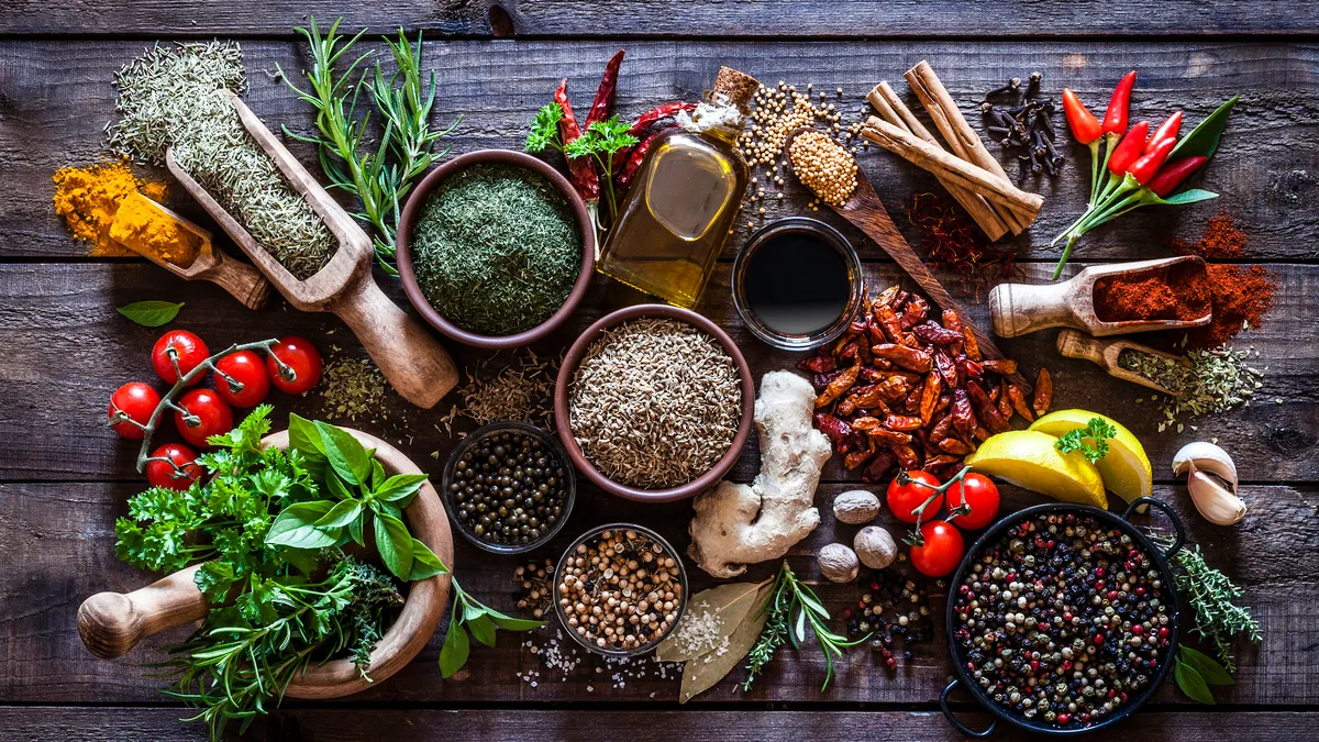 Several herbs, seasonings and spices in bowls and piles, grouped together on an old wooden table.