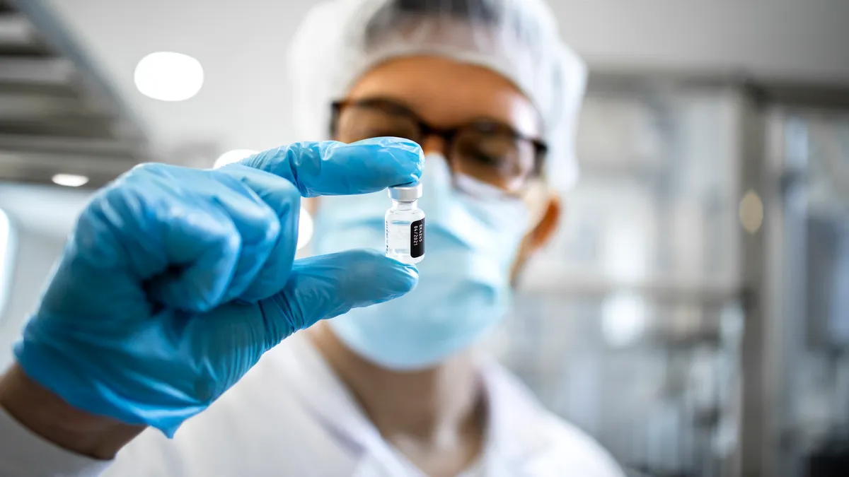 Pharmaceutical worker in protective equipment inspects product at a vaccine production facility.