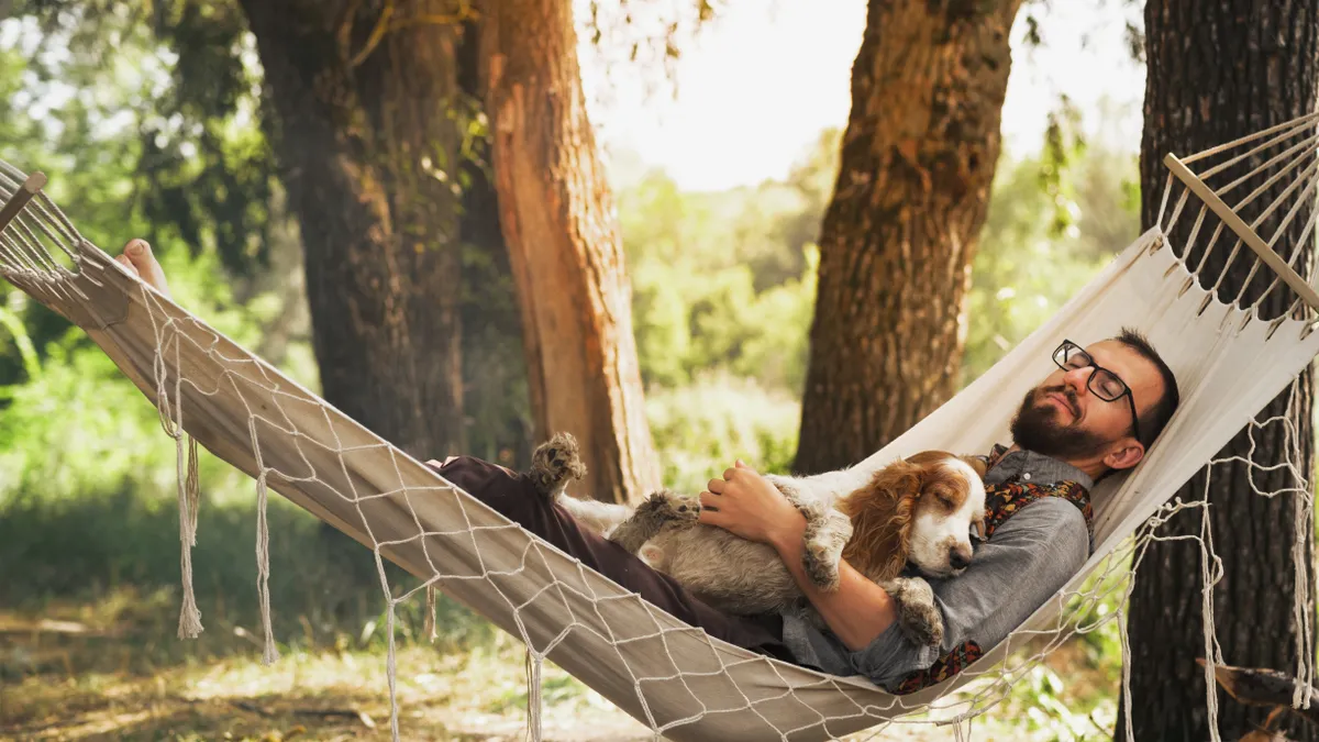 A man rests in a hammock with his dog.