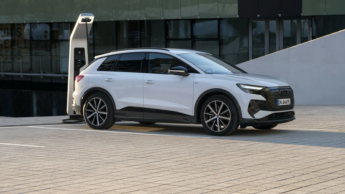 A white Audi Q4 40 e-tron electric SUV parked next to a charger with concrete building facade in the background.