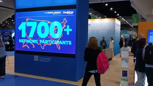 A digital sing at a conference shows the number 1700 under a FedNow logo, with attendees milling around.