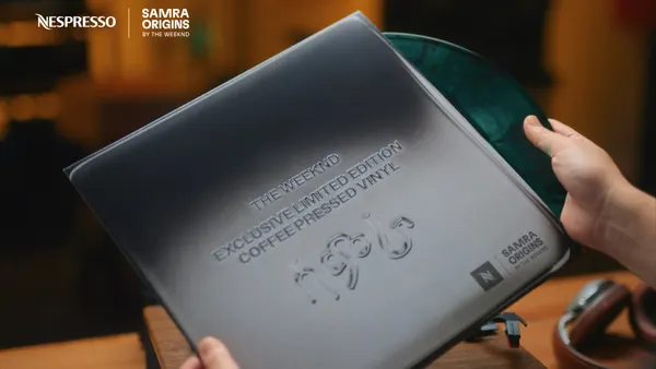 Hands hold the vinyl collaboration between The Weeknd and Nespresso, with the disc peaking out of the grey slip cover.
