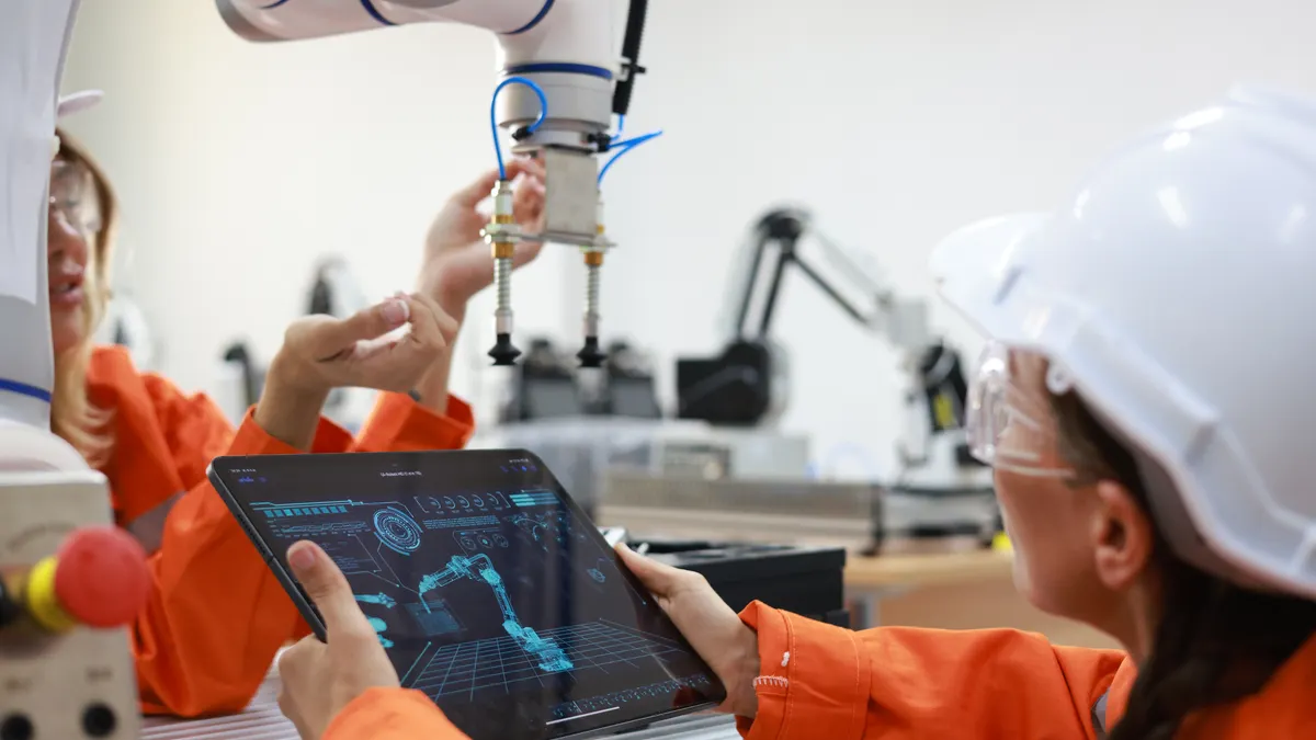 Two engineers work with a tablet to fix a robotic arm in a factory.