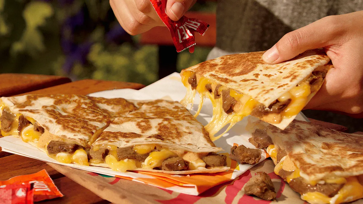 Hands put hot sauce on a large Taco Bell quesadilla made with chunks of plant-based Beyond Carne Asada.