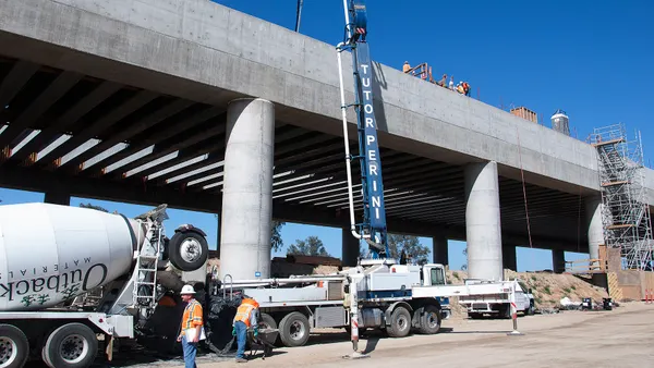 Workers walk a jobsite below an elevated high-speed rail track.